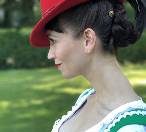 Model in Tracht mit PinCrown Tsavorit und roten Saphiren in Gelbgold gefasst Model in Tracht mit PinCrown Tsavorit und roten Saphiren in Gelbgold gefasst
